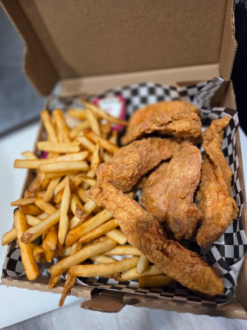 A box of golden chicken fingers with a side of fries